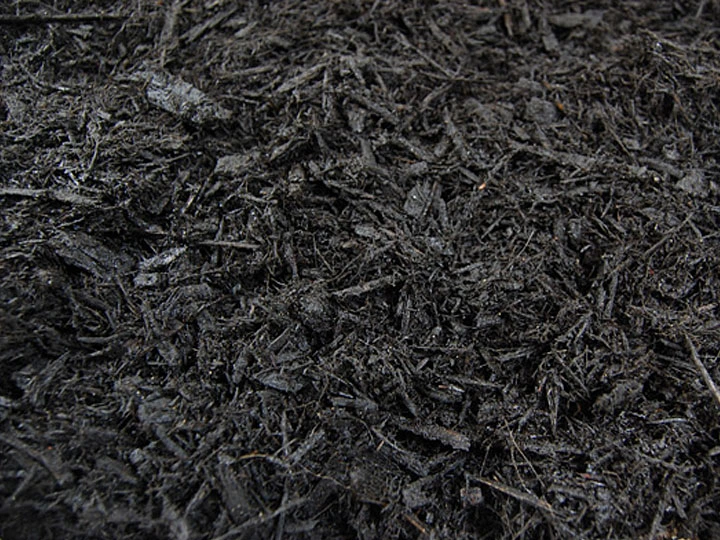 Close-up texture of dark black bark mulch pieces covering the ground